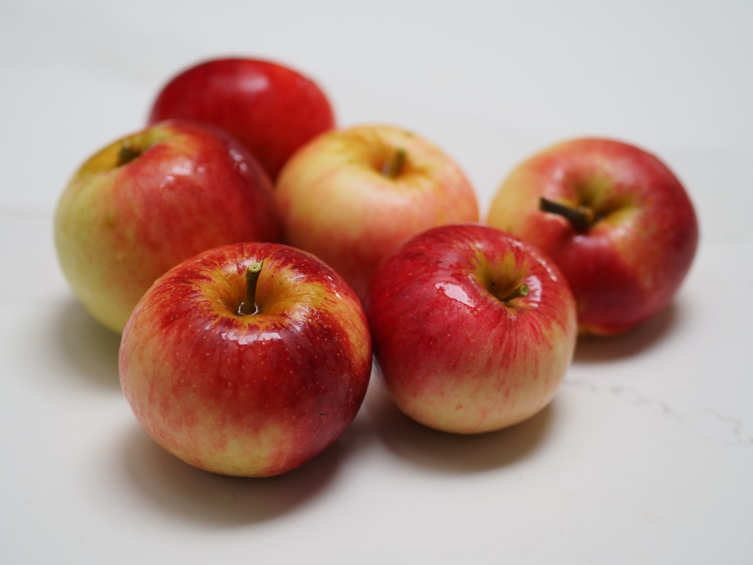 Six delicious-looking red and yellow-green apples on a white countertop.